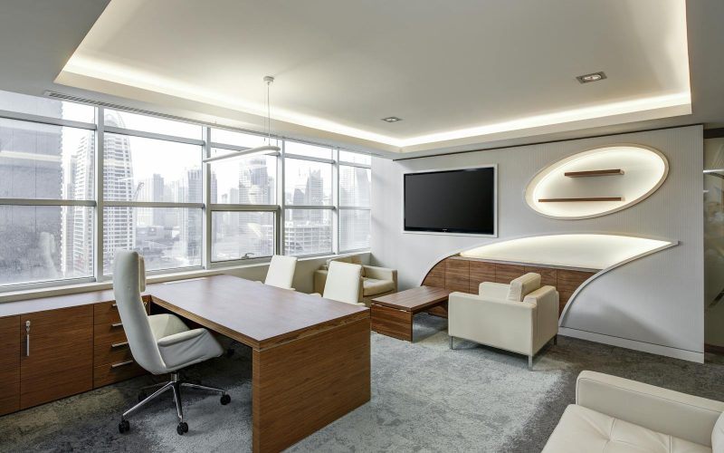 Gray Office Rolling Chair Near Brown Wooden Desk in Front of Flat Screen Tv on White Painted Wall