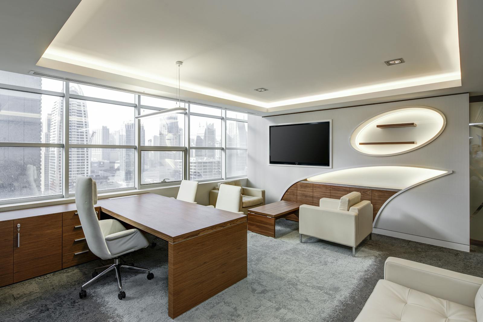 Gray Office Rolling Chair Near Brown Wooden Desk in Front of Flat Screen Tv on White Painted Wall