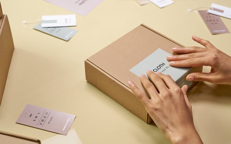 Hands carefully packing a cardboard box with multiple tags around, emphasizing sustainable packaging.