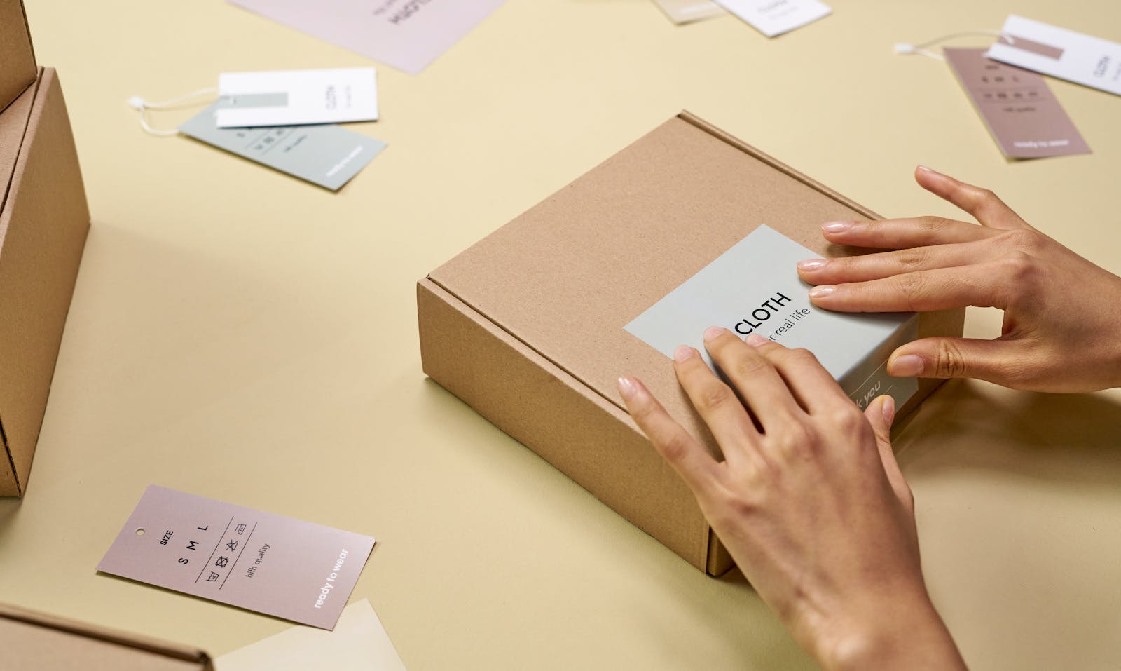 Hands carefully packing a cardboard box with multiple tags around, emphasizing sustainable packaging.